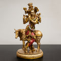 A golden sculpture of Lord Krishna sitting on a cow.