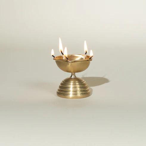 A gold colored, conical brass diya
