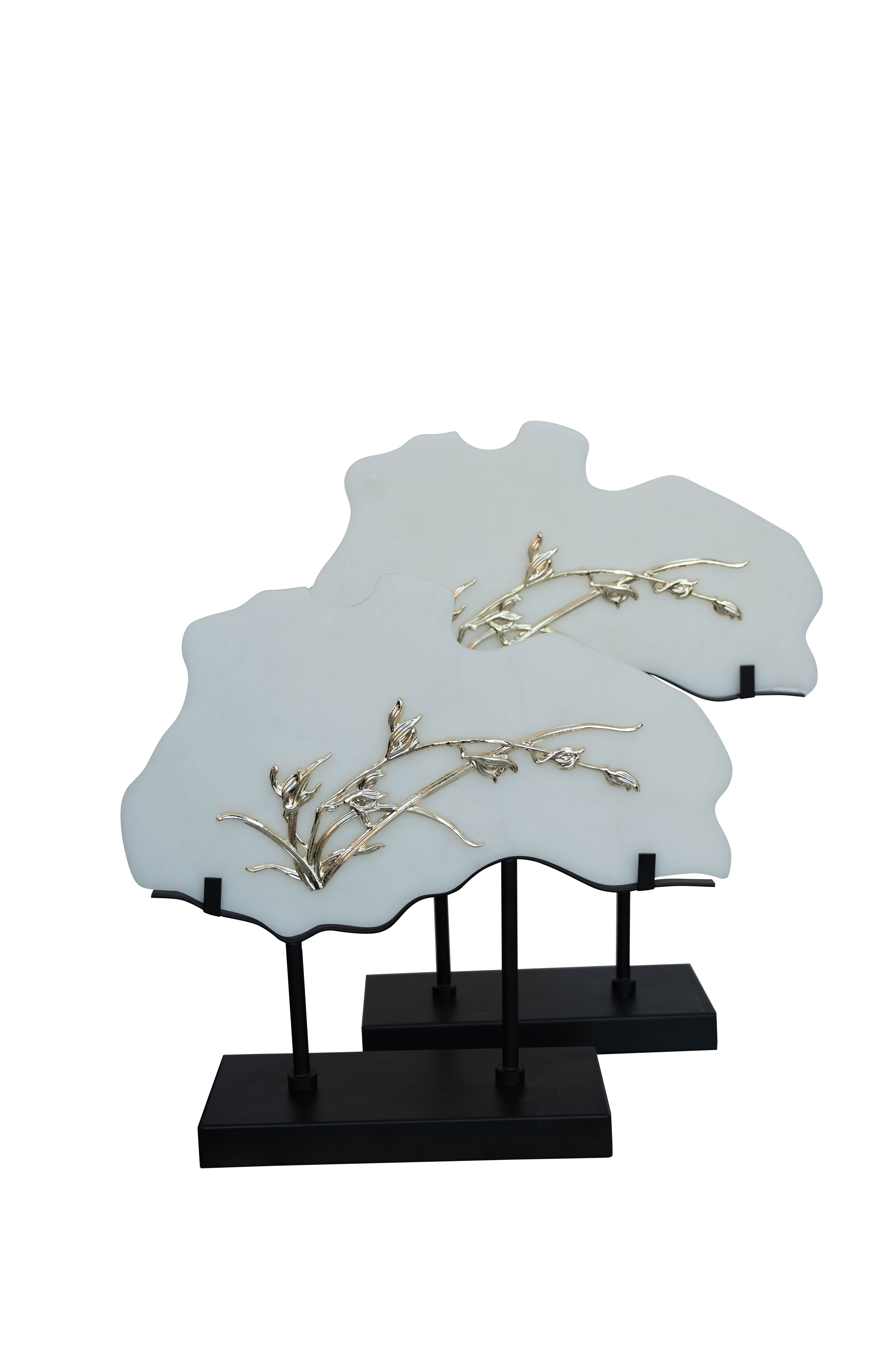 Two frame sculptures with white panels and gold detailing, with black metal stands.