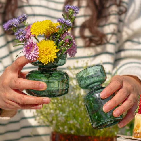 Person holding a green glass vase with flowers.