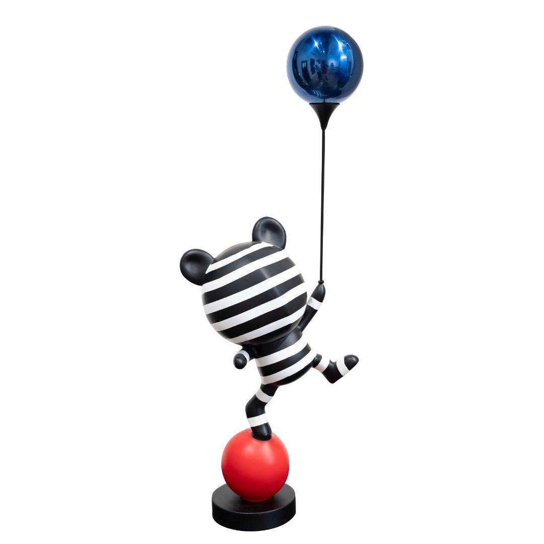 A whimsical cartoon bear sculpture with black and white stripes, holding a blue balloon