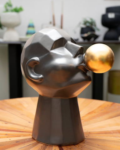 A black and gold ceramic sculpture of a face with a bubble gum ball. 