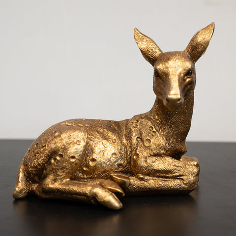 A golden sculpture of a deer with a lying pose.
