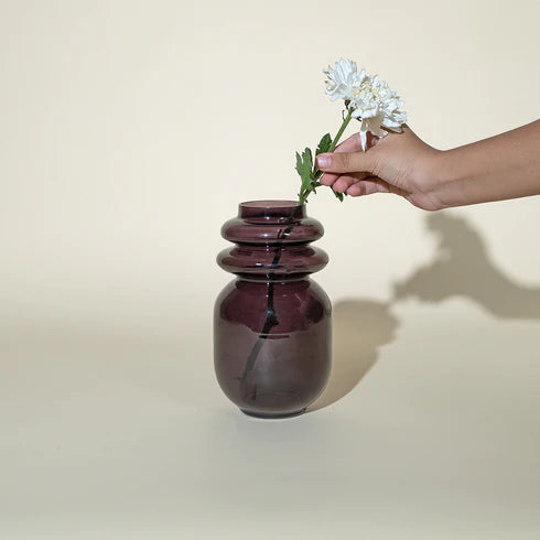 A person placing a white flower into a dark lilac colored glass vase.