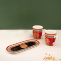 Two red and black ceramic mugs with a floral pattern and a matching platter 