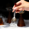 A hand holding a small glass bell with decorative elements