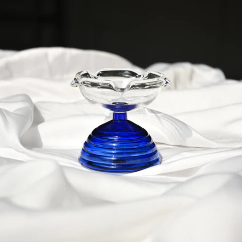 A clear glass diya with a blue glass base