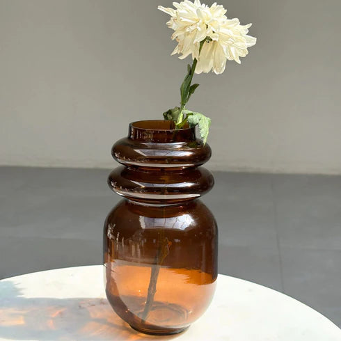A handcrafted haze brown loop glass vase with a flower