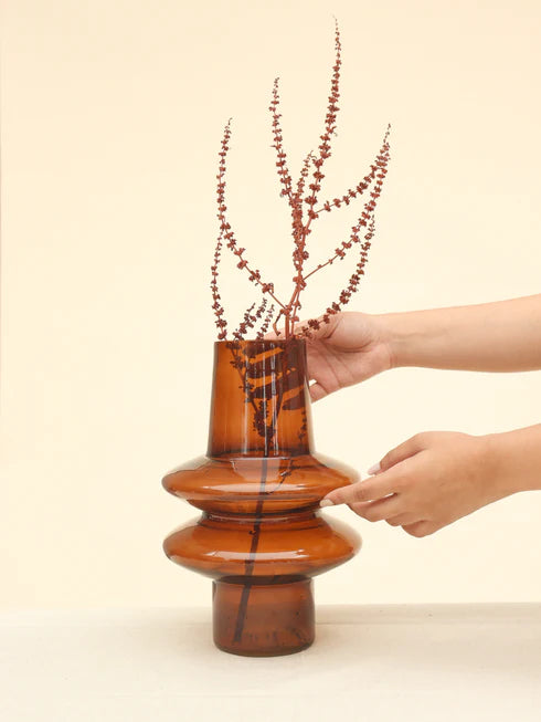 A person placing dried plants into a haze brown glass vase 