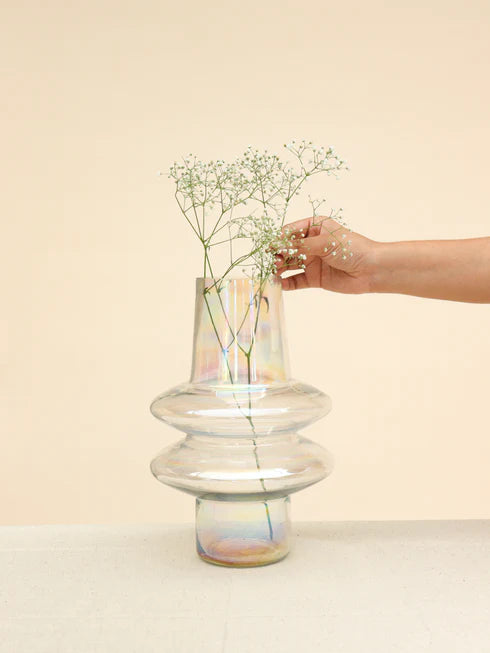 A hand placing a small branch with white flowers into aripple glass vase 